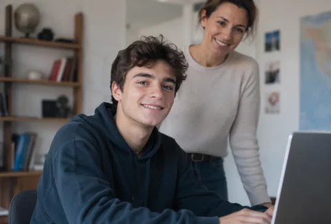Adolescent souriant devant son ordinateur, sa mère debout derrière lui