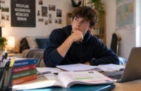 Lycéen réfléchissant devant ses manuels de mathématiques, physique-chimie et histoire-géographie